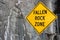 Large yellow and black sign warning pedestrians that it is a falling rock zone, to practice care when passing by