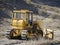 A large yellow bulldozer flattens a mountain dirt road in clouds of dust on a Sunny autumn day