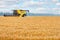 A large yellow combine harvester against the backdrop of a wheat field and a cloudy sky on a summer day