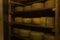 Large yellow heads of cheese on wooden shelves in a dark storage