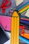 A large yellow paper pencil, next to a variety pencils, notebooks, clamps and crayons and other office supplies.