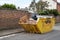 Large yellow skip full of bilding material waste on the street in an urban location