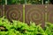 Laser cut rust color steel fence panels with spiral pattern and green shrub