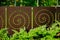 Laser cut rust color steel fence panels with spiral pattern and green shrub