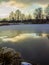 Late Autumn.Frosted pond under thin ice with coastal grass and shore covered with first snow with rare trees.