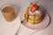 Late breakfast or dinner with lush pancakes sprinkled with powdered sugar, strawberries and tea in a glass mug on a light wooden