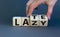 Late and lazy. Male hand flips wooden cubes and changes the word `lazy` to `late` or vice versa. Beautiful grey background, co