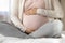 Late pregnant woman sitting in beddings, touching, caressing baby bump