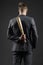 Latent aggression. Businessman or man in formal suit hides wooden bat behind back, dark background. Hidden danger