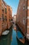 Lateral canal with docked boats in Venice, Italy. Reflections and ble sky