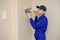 Lateral view of a young electrician in blue overall disassembling a electrical panel