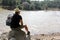 Latin adult man with hat and sunglasses sitting on a stone next to a lake makes the victory sign happy, accomplished, with achieve