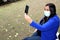 Latin adult woman with protection mask on video call with her mobile and headphones in the park, new normal covid-19