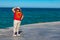 Latin American woman standing at tourist viewpoint, sea in background against blue sky