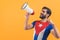 Latin bearded man dressed in Cuban flag t shirt screaming to megaphone over orange studio background