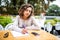 Latin curly female student writing in copybook at sidewalk cafe. Portrait of Caucasian woman wearing white T-shirt sitting at tabl