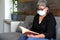 Latin grandmother with protection mask reading book in waiting room