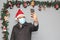 Latin man with protection mask, coat and Santa Claus hat in video call with cell phone and Christmas decoration, new normal covid