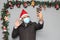 Latin man with protection mask, coat and Santa Claus hat in video call with cell phone and Christmas decoration, new normal covid