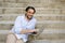 Latin man sitting on city staircase working with laptop computer looking satisfied and confident