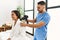 Latin man and woman wearing physiotherapy uniform massaging neck using percussion gun at beauty center