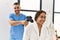 Latin man and woman wearing physiotherapy uniform massaging neck using percussion gun at beauty center