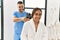 Latin man and woman wearing physiotherapy uniform massaging neck using percussion gun at beauty center