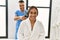 Latin man and woman wearing physiotherapy uniform massaging neck using percussion gun at beauty center