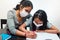 Latin mother helps her daughter with the homework on a black table at home, wears prevention mask. Teleworking and studying at