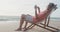 Latin senior hispanic man relaxing on sunbed on beach at sunset, using smartphone