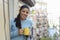 Latin woman drinking cup of coffee or tea smiling happy at apartment window balcony