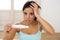 Latin woman holding pregnancy test on bed at home looking at positive result in shock and stress