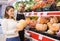 Latin woman with orange pumpkin in supermarket and shop employee working near