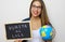 Latin young female teacher holding globe and blackboard with spanish written