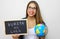 Latin young female teacher holding globe and blackboard with spanish written