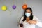 Latina with black hair with protection mask, cake, colored balloons celebrates birthday at home by quarantine and new normal covi