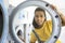 Latina woman looking through the glass of a washing machine in a public self-service laundromat