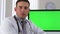 Latino doctor sitting with green screen on computer in background