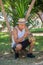 Latino man playing the trumpet crouched near a plant outdoors