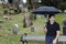 Latino man sits with umbrella on bench in cemetery