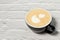 Latte art on cappuccino in a black Cup on a white brick background. side view of the Cup close-up, latte art in the shape of a