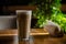 Latte in a tall transparent glass on a wooden cafe table, with green tree in the background, with napkins nearby