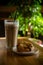 Latte in tall transparent glass on wooden cafe table on sunny day, tree in background, saucer with cookies nearby