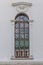 Lattices on a narrow long window in the white wall of the temple. Exterior. Vertical