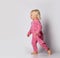 Laughing barefooted blonde baby kid girl in pink warm comfortable jumpsuit is running aside over grey wall background