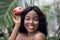 Laughing black woman with fresh red pomegranate. Photo of pleasant afro woman with nude makeup on tropic palms