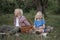 Laughing boy and little girl wicker basket in hand sit on lawn in garden. Picnic for children on warm summer day