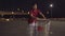 Laughing cheerful Caucasian man having fun with shopping cart on empty parking lot at night. Portrait of young handsome