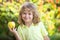 Laughing cute blond little child boy eating big apple fruit. Kids portrait on blurred nature background.