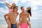 Laughing fellows in swimming trunks holding beautiful girls on a seashore on a blurred natural background.